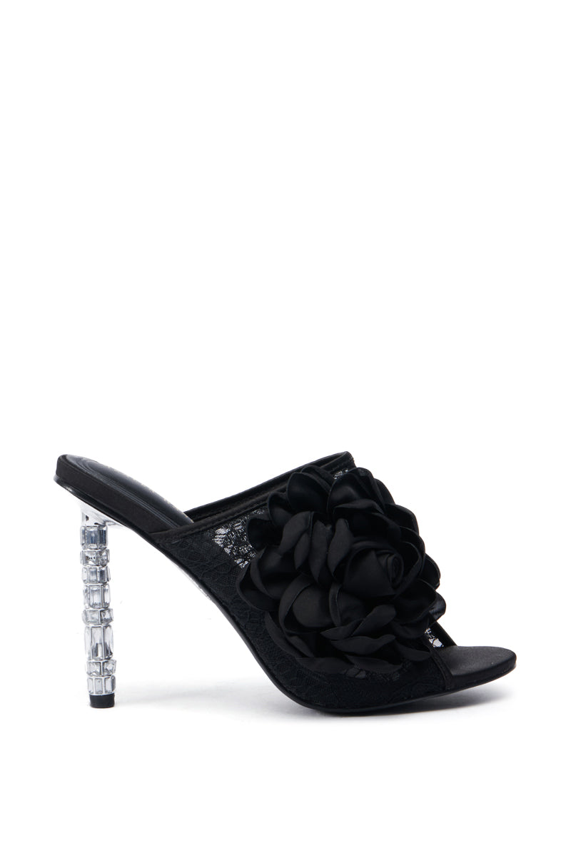 Introducing the AZALEA WANG URMI BLACK SANDAL: This high-heeled shoe boasts a striking large black flower applique on the front strap. The clear heel features a geometric pattern, offering a stylish and modern contrast to the chic lace black fabric of this sandal.