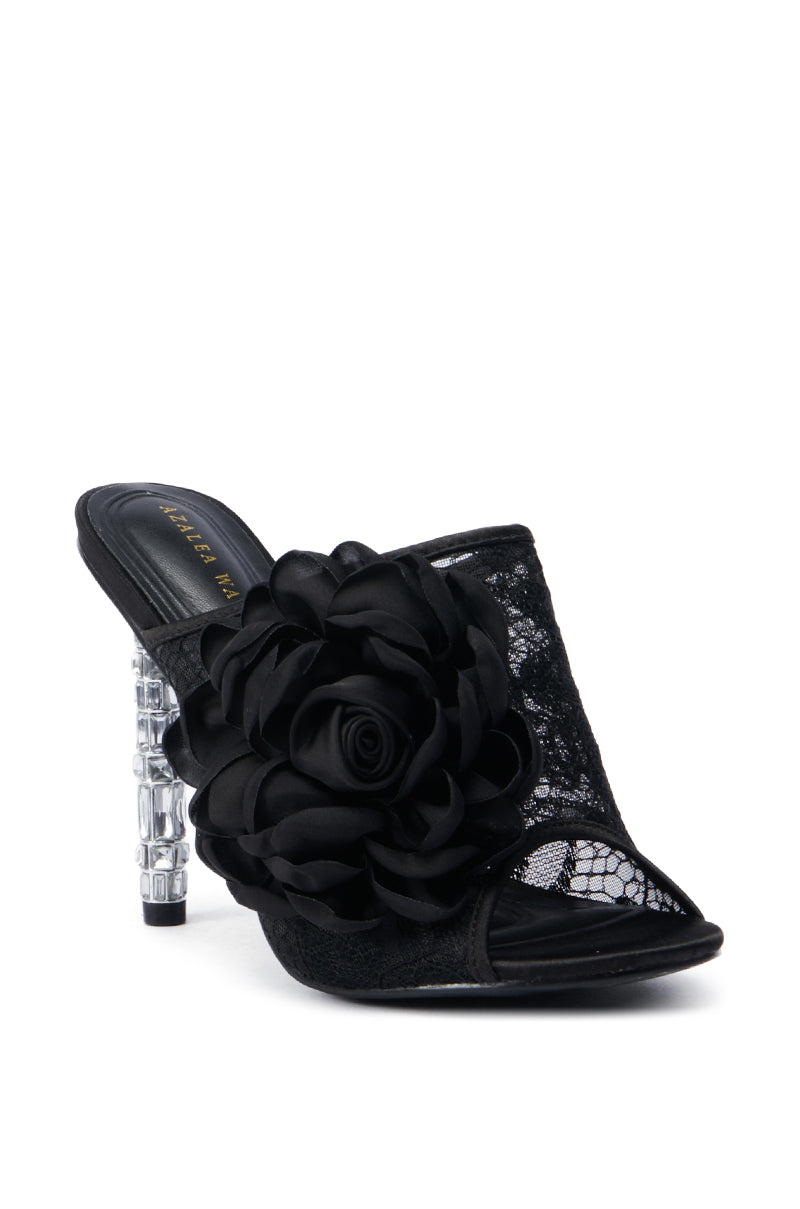 The AZALEA WANG URMI BLACK SANDAL is a chic high-heeled lace sandal with a clear heel, accentuated by black lace detailing and adorned with a prominent black rose on the side. The partially open front elegantly displays its design, while the comfort cushion insole ensures added ease.
