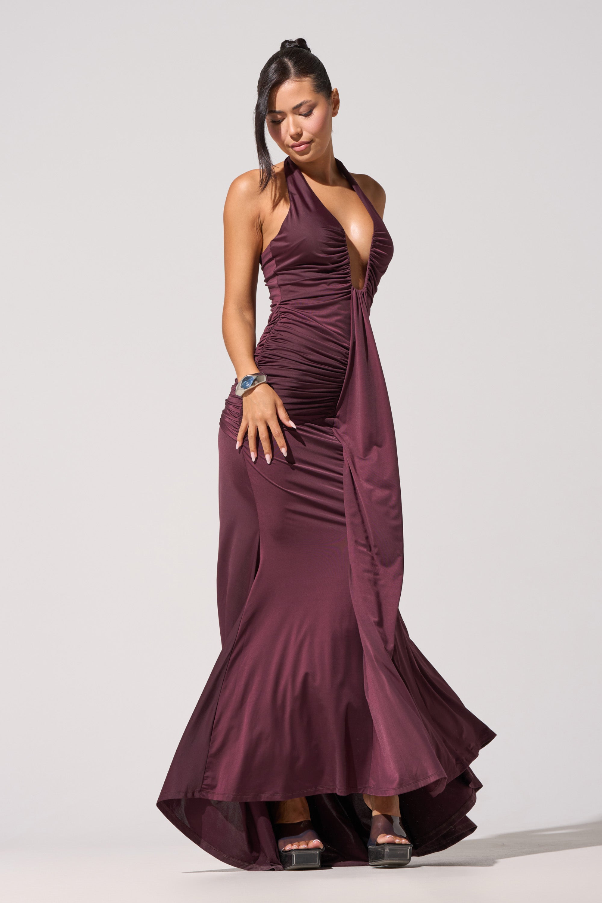 A woman poses against a plain background, looking down with one hand on her hip, wearing the SET THE MOOD MESH HALTER MAXI DRESS, paired with platform heels and a bracelet. 1