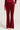 A person wearing the Velour Galore Flared Leg Jogger in burgundy with large front pockets and white sneakers stands against a plain background. The joggers feature a wide-leg design and are paired with a matching red top.