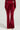 A person wearing the Velour Galore Flared Leg Jogger in Burgundy stands against a plain background. These joggers feature flared legs, two front flap pockets, and a wide-leg fit, complemented by a matching waistband in the same color as they rest their hands at their sides.