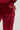 A person is dressed in the Velour Galore Flared Leg Jogger in Burgundy, showcasing the back pocket of the pants with a noticeable button feature. The fabric looks soft and plush, emphasizing its luxurious texture.