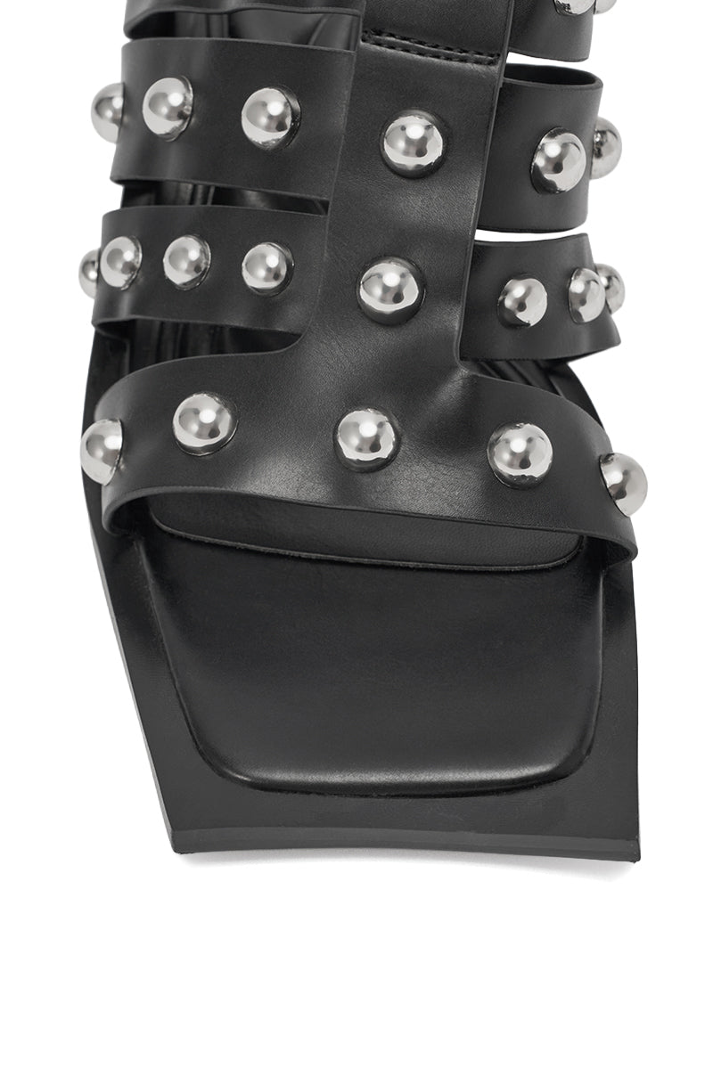Close-up of the AZALEA WANG VANDAL BLACK NOVELTY HEEL SANDAL with a square toe, black faux leather straps embellished with large silver studs, and a striking silver metallic block heel. 7