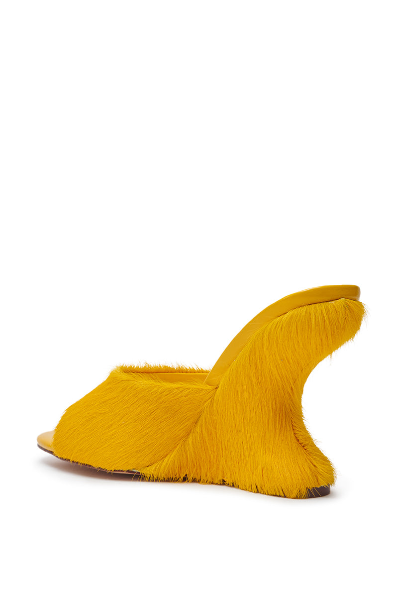 The AZALEA WANG VASA MUSTARD OPEN TOE SANDAL is a bright yellow mule with a wedge heel and textured faux fur, shown from the rear side against a white background.
