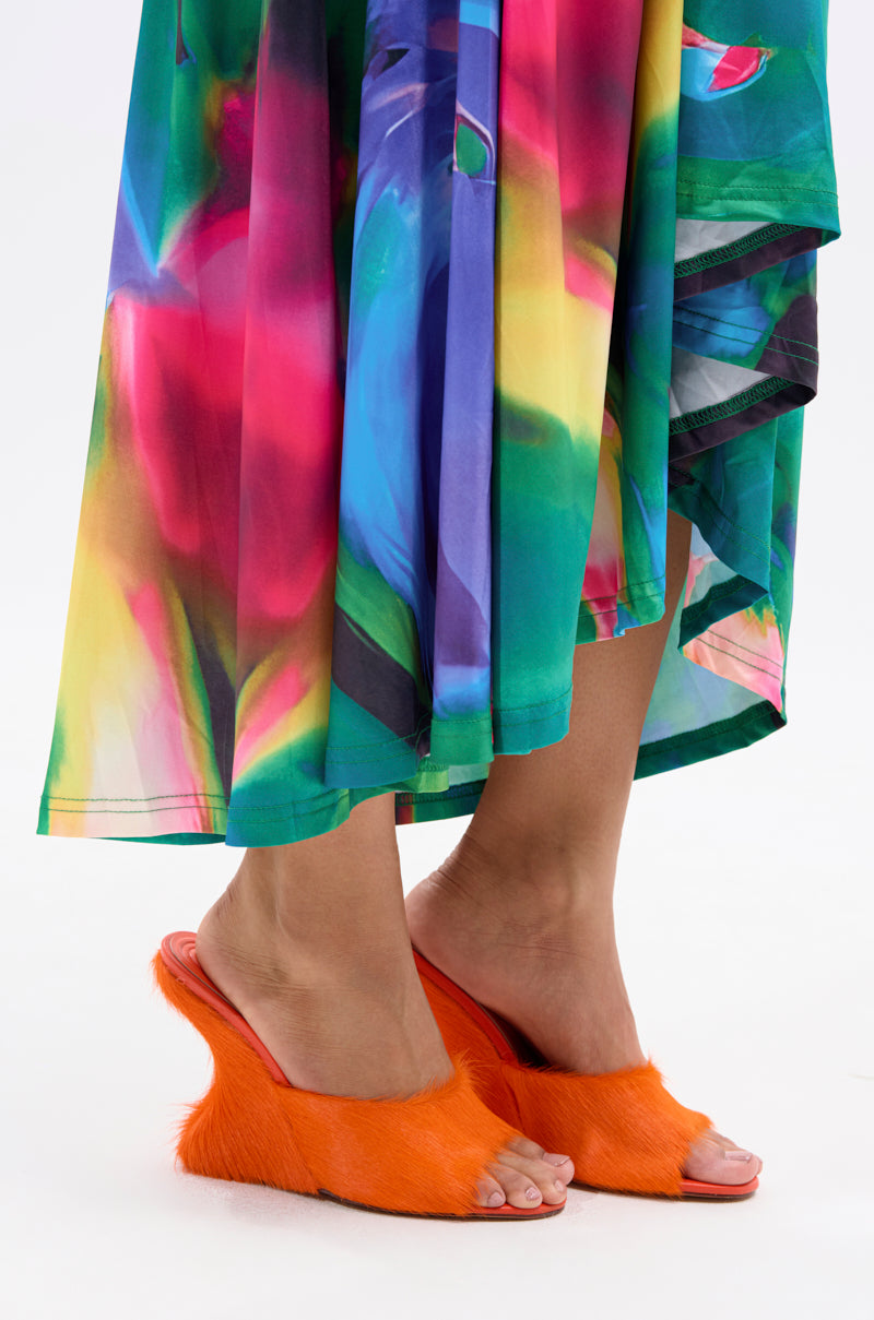 Against a white background, a person wears a colorful abstract-patterned skirt and AZALEA WANG VASA ORANGE FURRY WEDGE SANDALS featuring bright orange fur and an open almond toe. 1