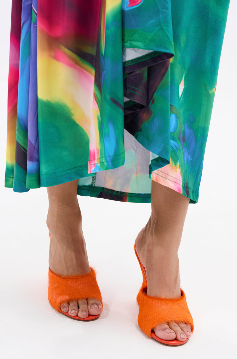 A person stands on a white surface, wearing a colorful flowy skirt and the AZALEA WANG VASA ORANGE FURRY WEDGE SANDAL, featuring bright orange faux pony hair and an open almond toe design. 2