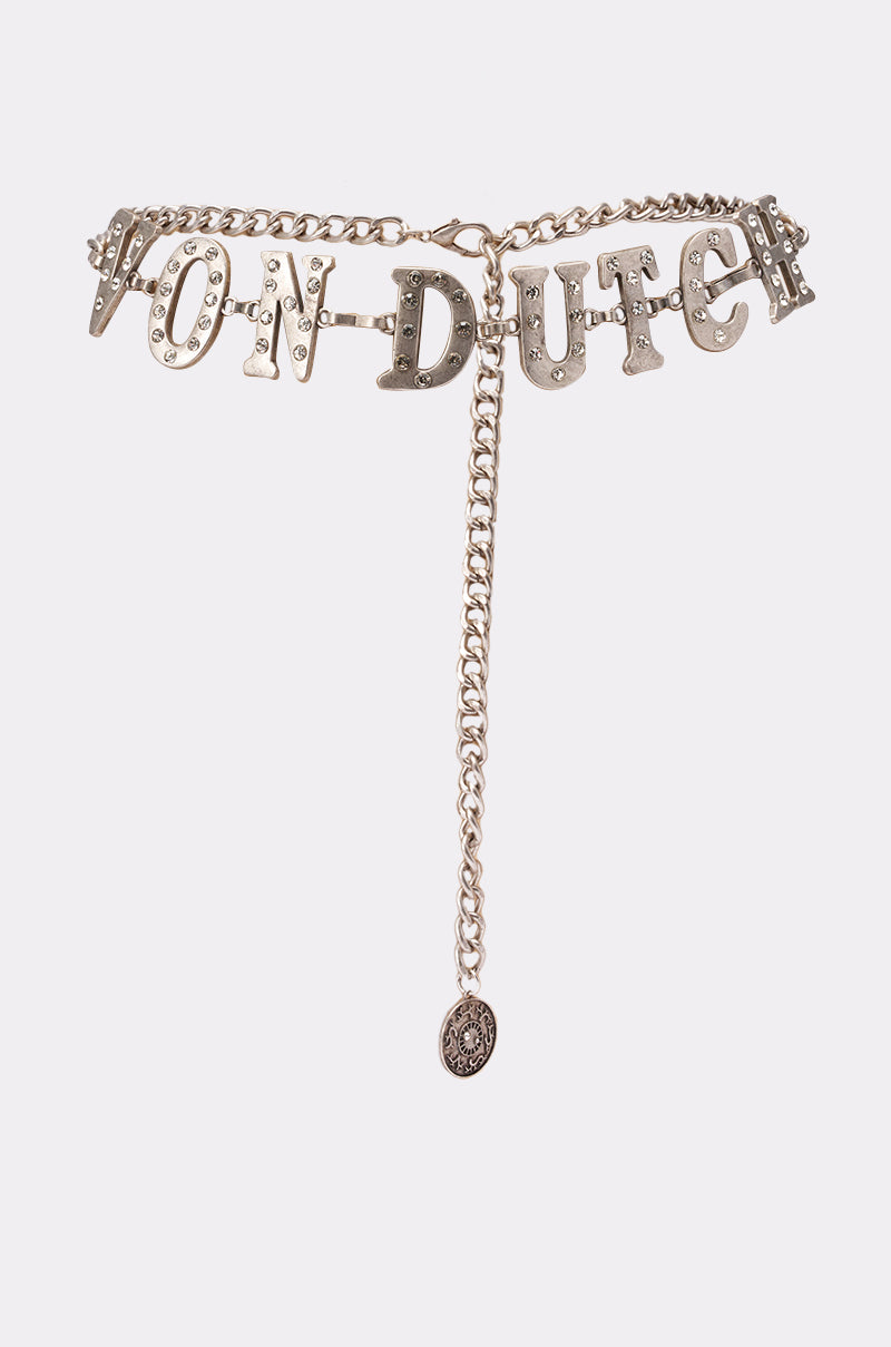 The VON DUTCH RHINESTONE CHAIN BELT features large silver letters, sparkling rhinestones, and a dangling medallion for a bold festival look. Shown on a plain white background. 1