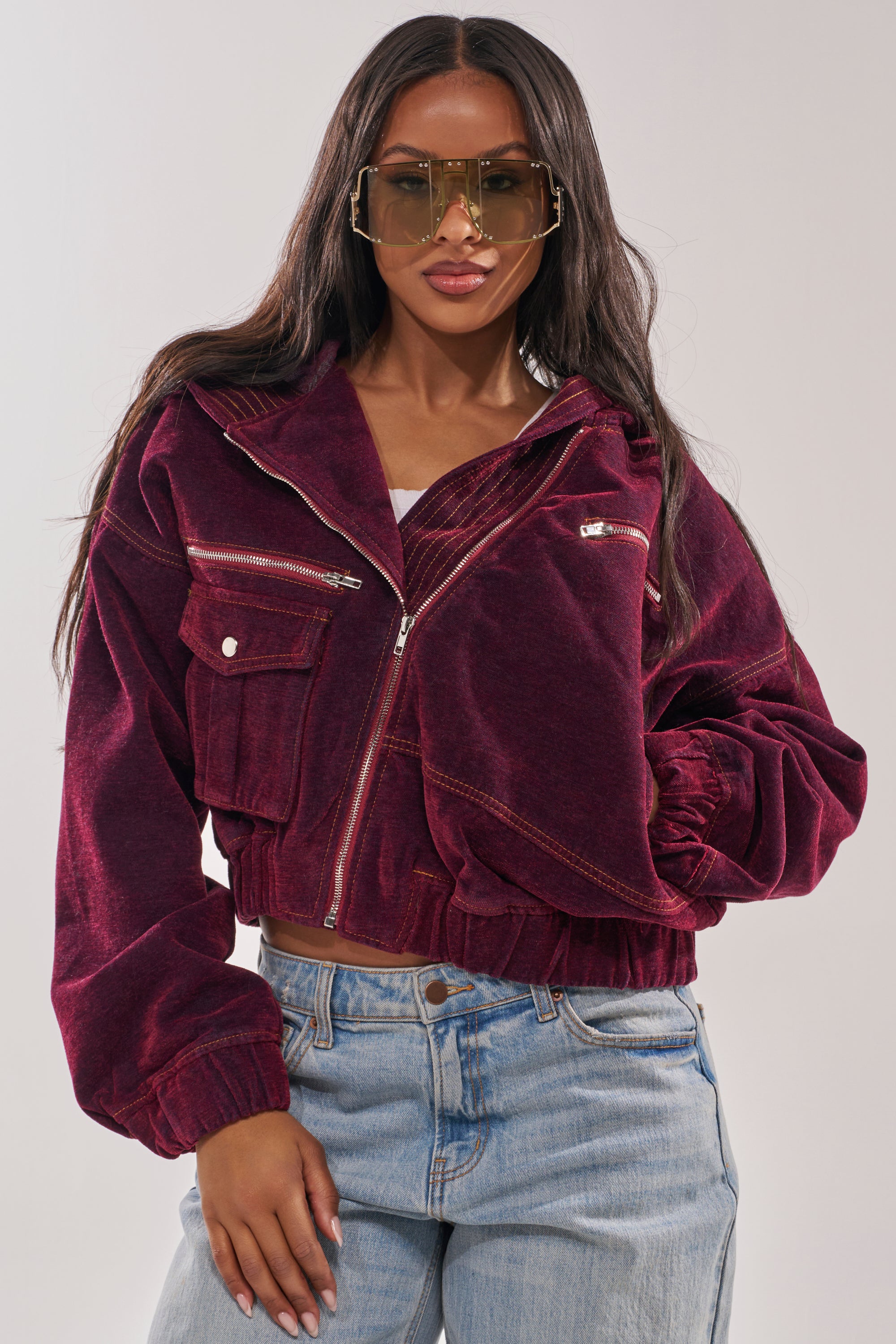 A woman in oversized sunglasses and the PAYTON VELVET DENIM BOMBER, paired with light blue jeans, stands confidently against a plain background. 1