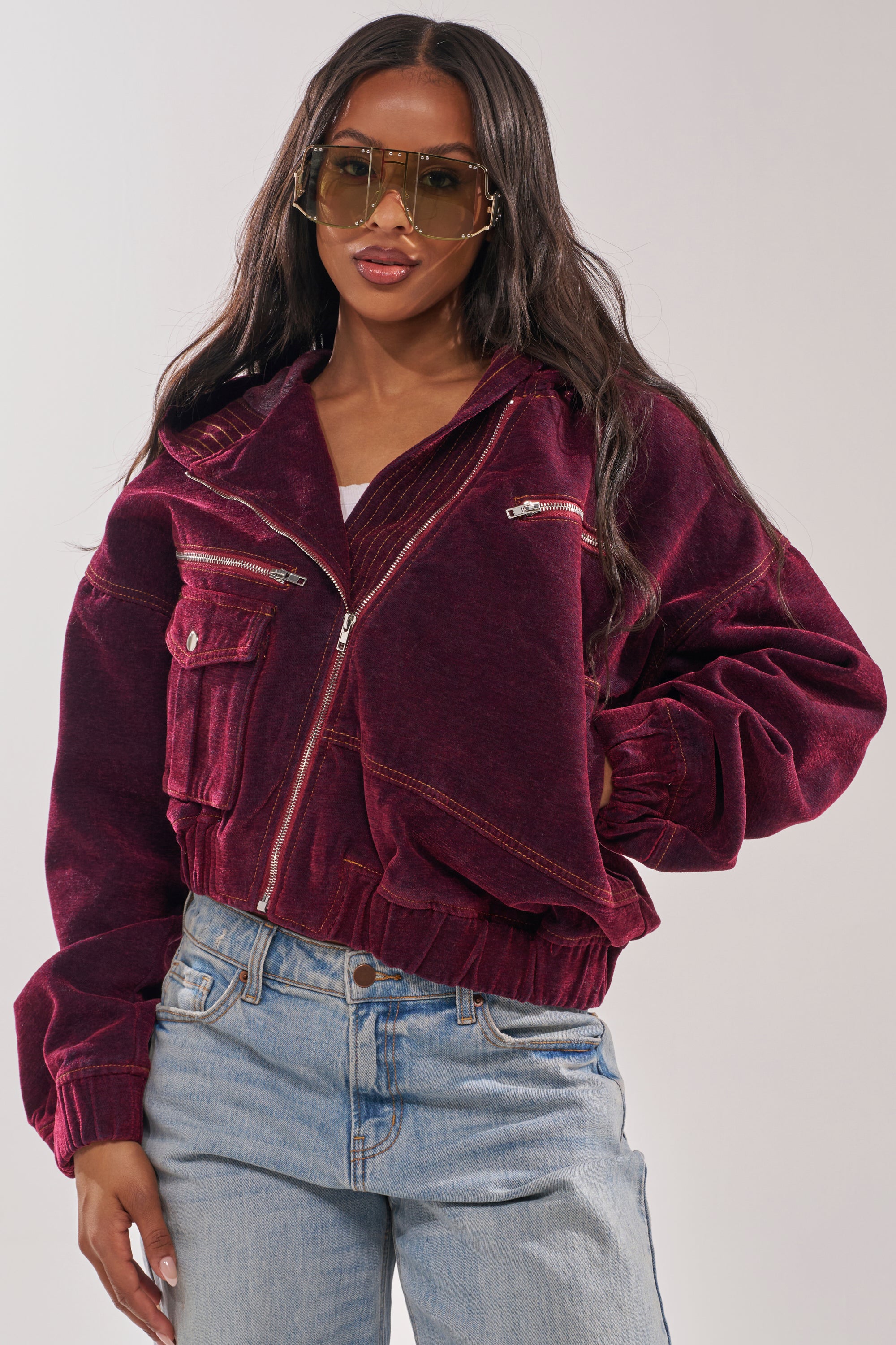 A woman in oversized sunglasses and the PAYTON VELVET DENIM BOMBER with multiple pockets pairs it with light blue jeans, posing confidently against a plain background. 3