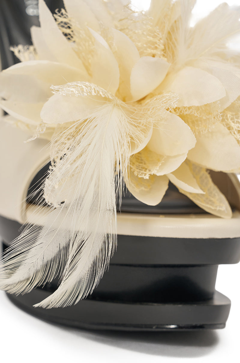 Close-up of the AZALEA WANG VELVETINE IVORY STILETTO PLATFORM SANDAL, showcasing its cream faux leather upper with a flower and feather embellishment on a platform stiletto heel. 6
