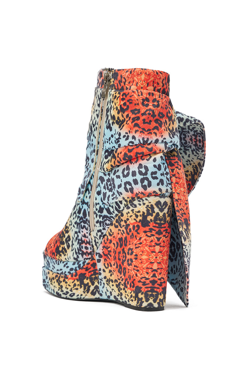 The AKIRA GOLD VENEZIO MULTI COLOR CHEETAH PRINT WEDGE BOOTIE features a vibrant cheetah print in red, blue, orange, and black, with a platform wedge heel, side zipper, and an exaggerated bow detail at the back. 6