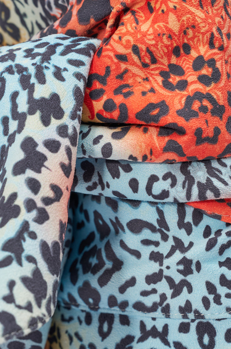 Close-up of layered, soft fabric with bold black cheetah spots on light blue and orange, inspired by the AKIRA GOLD VENEZIO MULTI COLOR CHEETAH PRINT WEDGE BOOTIE. The material looks slightly textured and eye-catching. 7