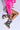 Person sits on the floor wearing a bright pink fur jacket, patterned skirt, and AZALEA WANG VENEZIO MULTI BOOTIE. Legs are crossed against a neutral background, radiating neon dreams in every technicolor print.