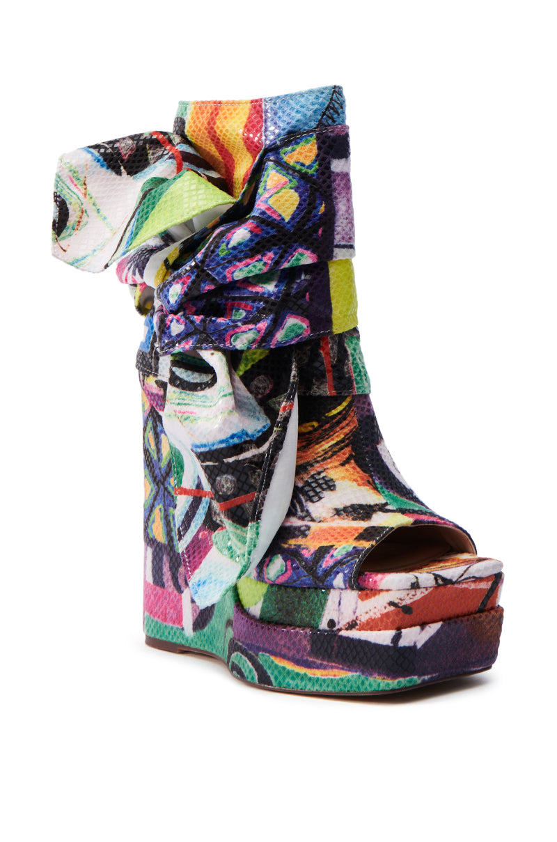 The AZALEA WANG VENEZIO MULTI BOOTIE features a vibrant abstract technicolor print with an open toe and a chunky wedge heel, complete with a wrapped fabric ankle detail.