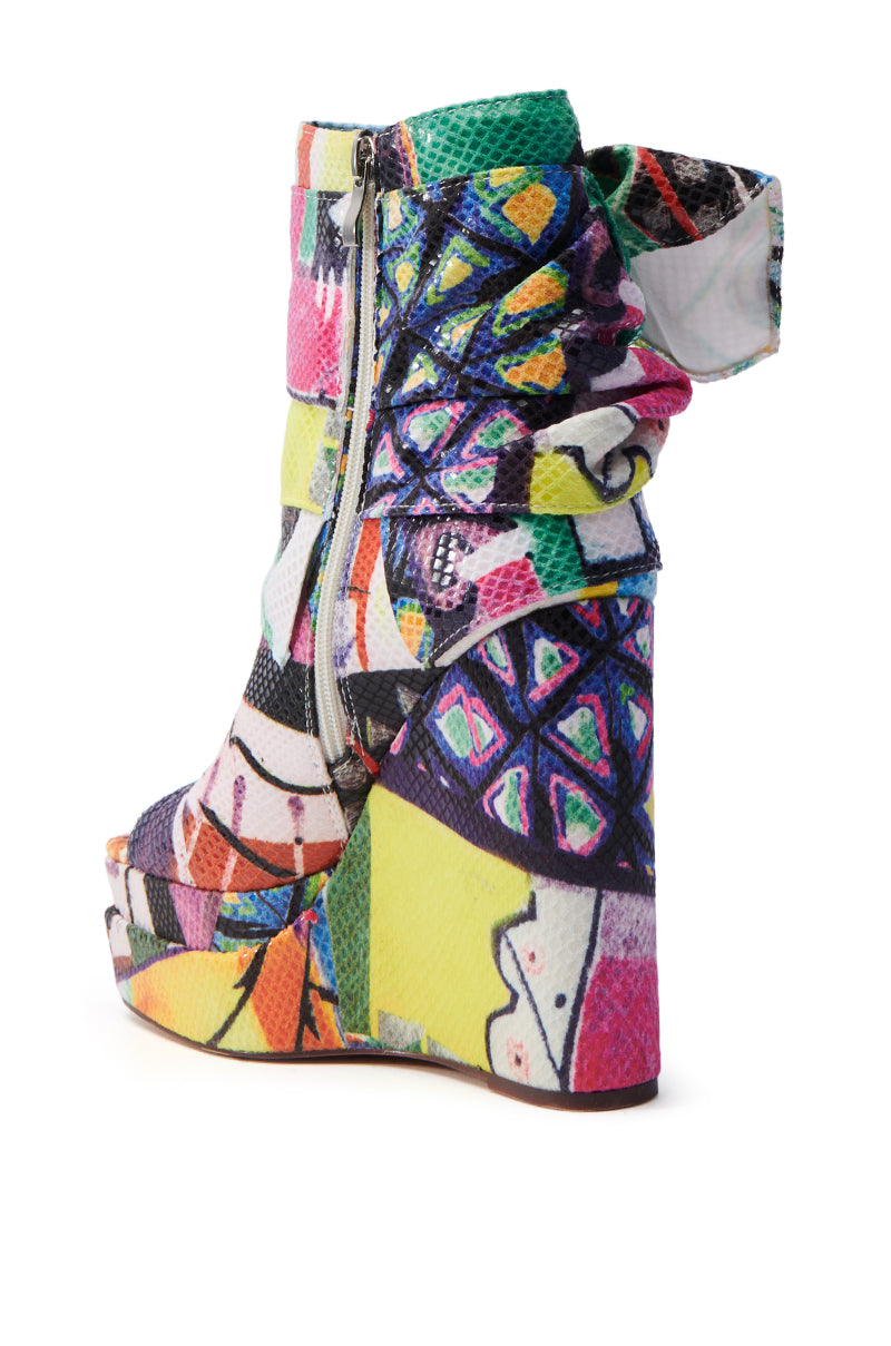 The AZALEA WANG VENEZIO MULTI BOOTIE is a colorful wedge shoe featuring a geometric pattern, chunky wedge heel, high ankle collar, side zipper, and technicolor print with vibrant abstract shapes in purple, yellow, green, and pink.