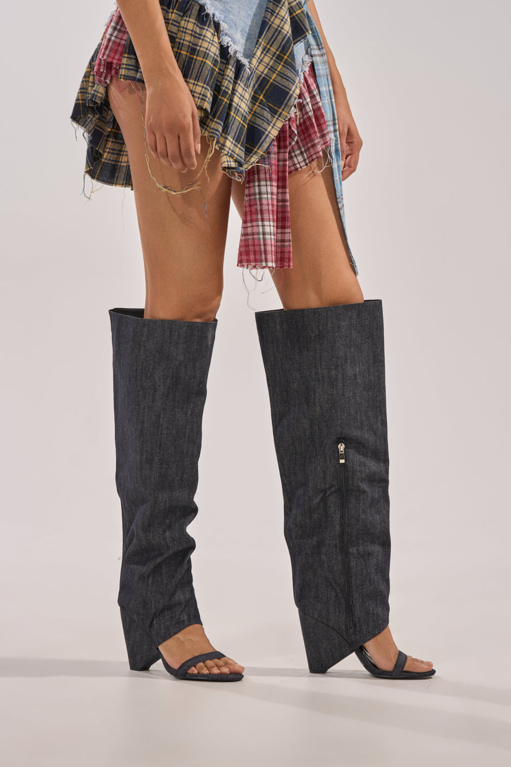 A person in a patchwork plaid mini skirt wears AZALEA WANG VEONA DARK DENIM OVER THE KNEE CHUNKY HEEL SANDALS with open toes and heels, standing against a plain background. 3