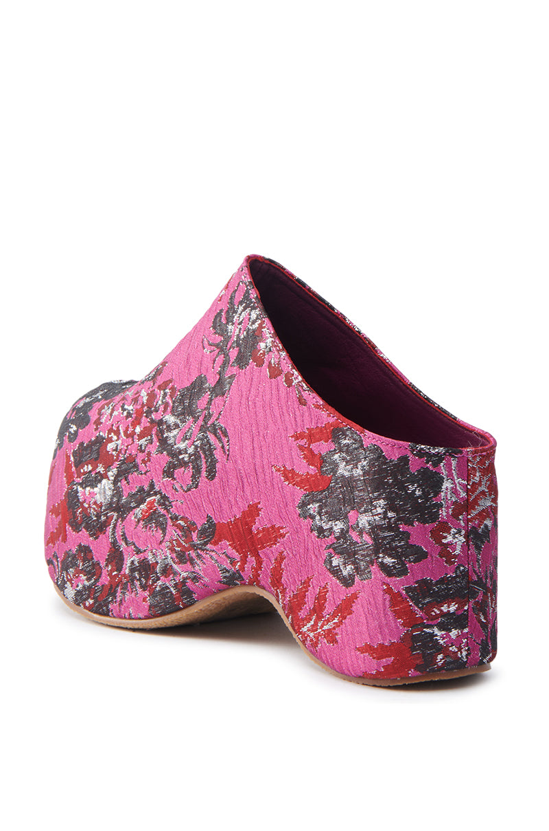 The AZALEA WANG Vesta Pink Multi Brocade Clog is an artistic masterpiece, showcasing a vibrant floral brocade pattern in pink, black, and red. This sculptural shoe features a high wedge heel, closed back, and platform sole that enhance its textured elegance.
