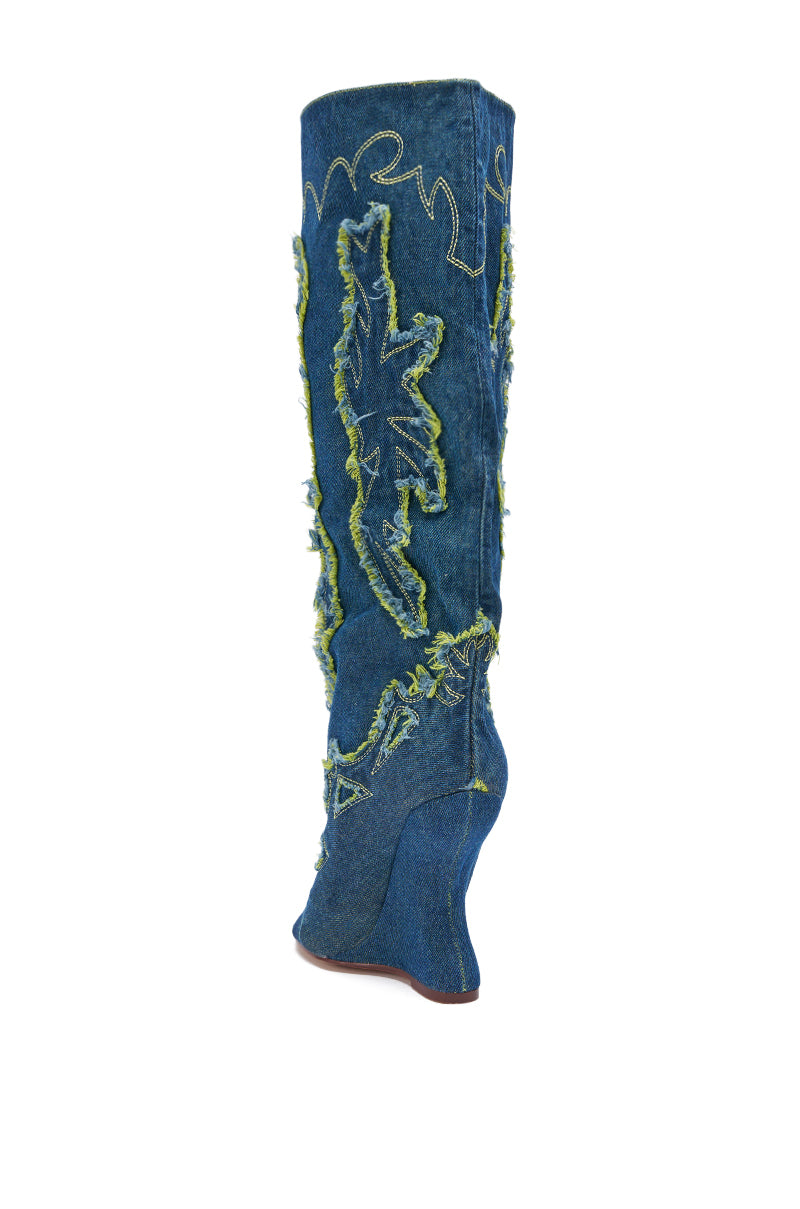 The AZALEA WANG VIANCA GREEN MULTI DENIM WEDGE BOOT features knee-high denim, green frayed applique, and decorative white stitching for a trendy Western look. The boot is shown at a slight angle in the photo.