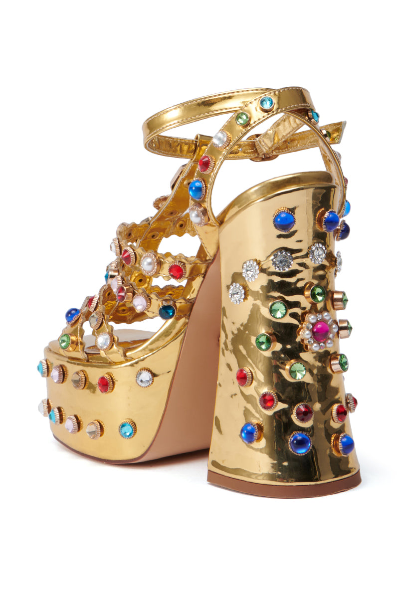 AZALEA WANG VIANNI GOLD CHUNKY SANDAL features a gold design with a thick block heel and is embellished with multicolor gemstones. It also includes intricate cut-out patterns and an ankle strap, highlighting vibrant details in red, blue, green, and white hues.