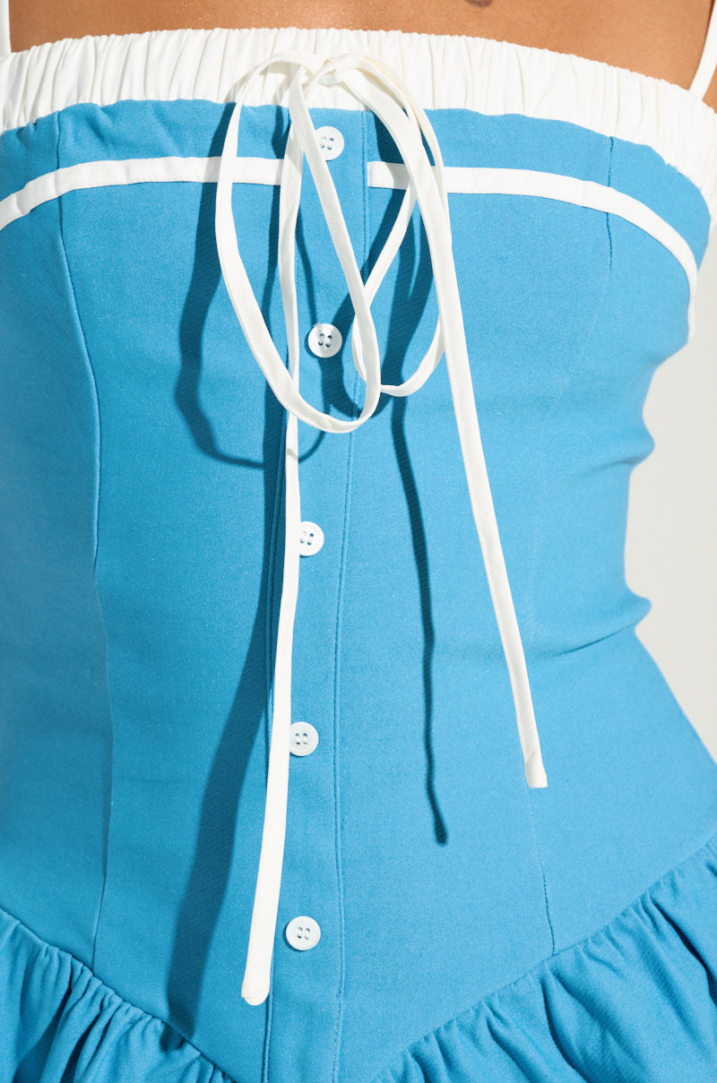 Close-up of a person wearing the TOO SWEET POPLIN MINI DRESS, which features a corset-inspired bodice with a white drawstring. The blue dress is designed with buttons down the front and a white trim across the chest, flowing elegantly into a subtly flared skirt.
