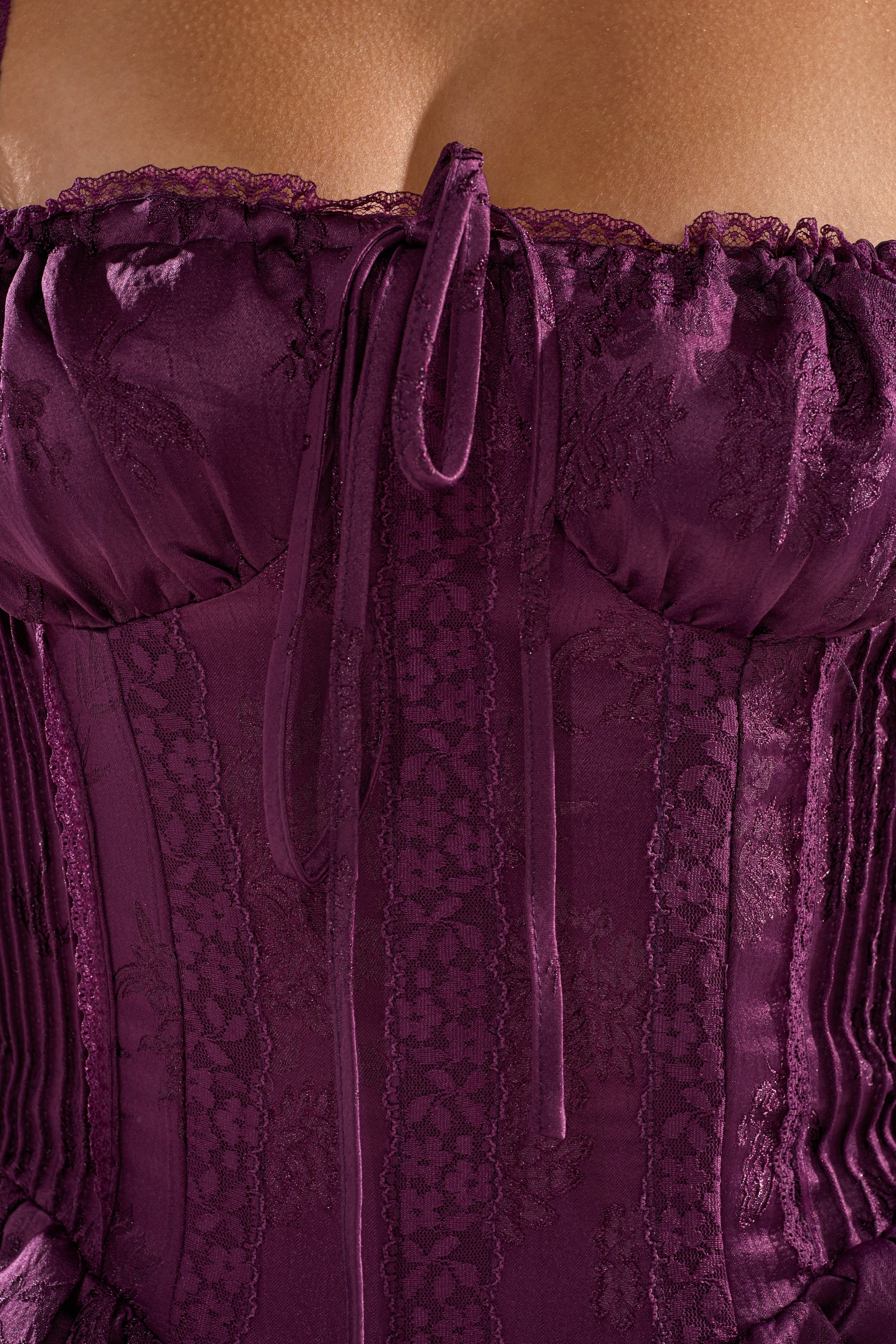 Close-up of a person wearing the DANCE WITH ME MINI DRESS IN PLUM, featuring a deep purple corset-style bodice with satin ribbon tie and intricate floral patterns, highlighting the neckline and upper chest. 8