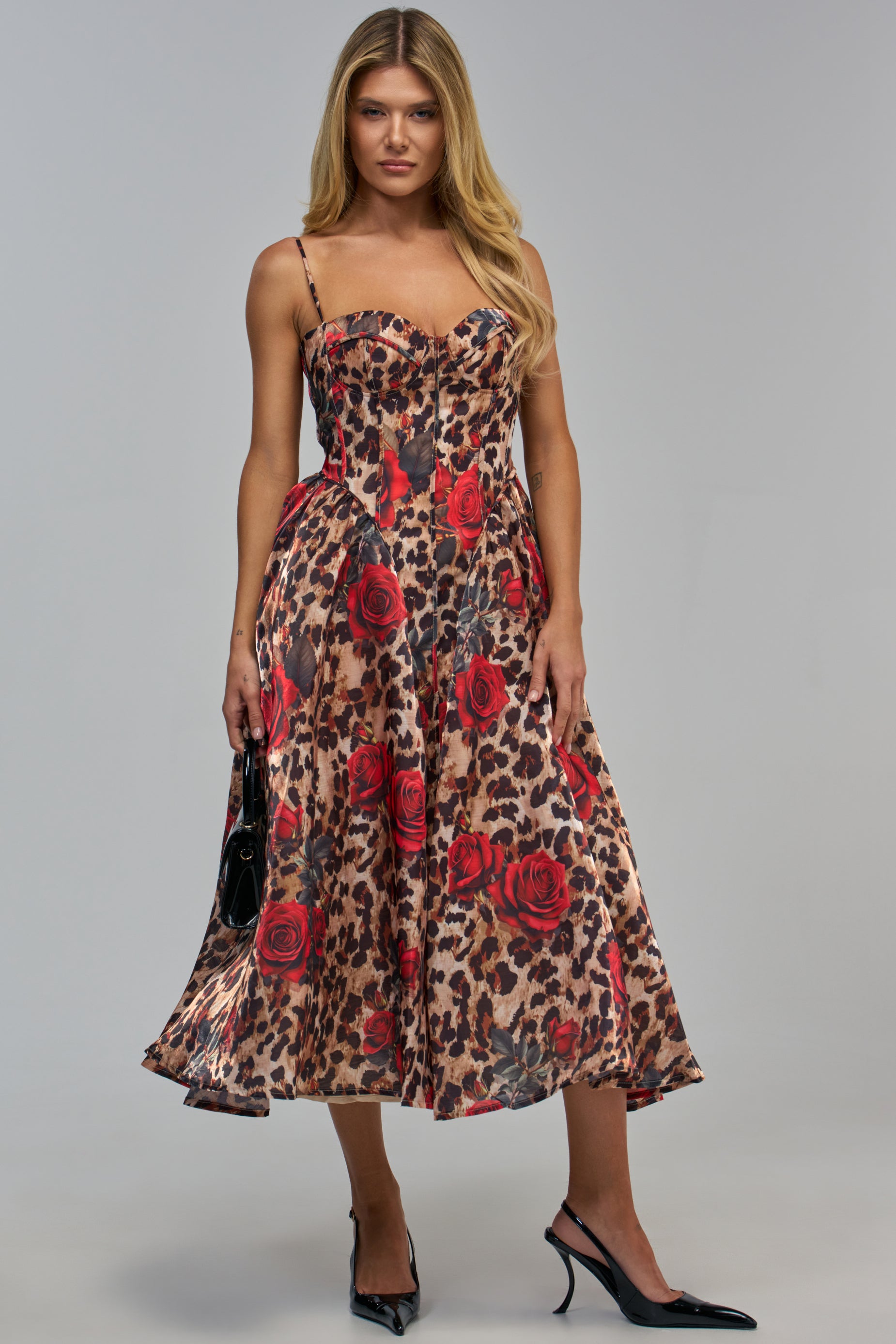 A woman wears the TROUBLE MAKER LEOPARD FLORAL MIDI DRESS, a sleeveless leopard print design with a corset-style bodice featuring red roses.