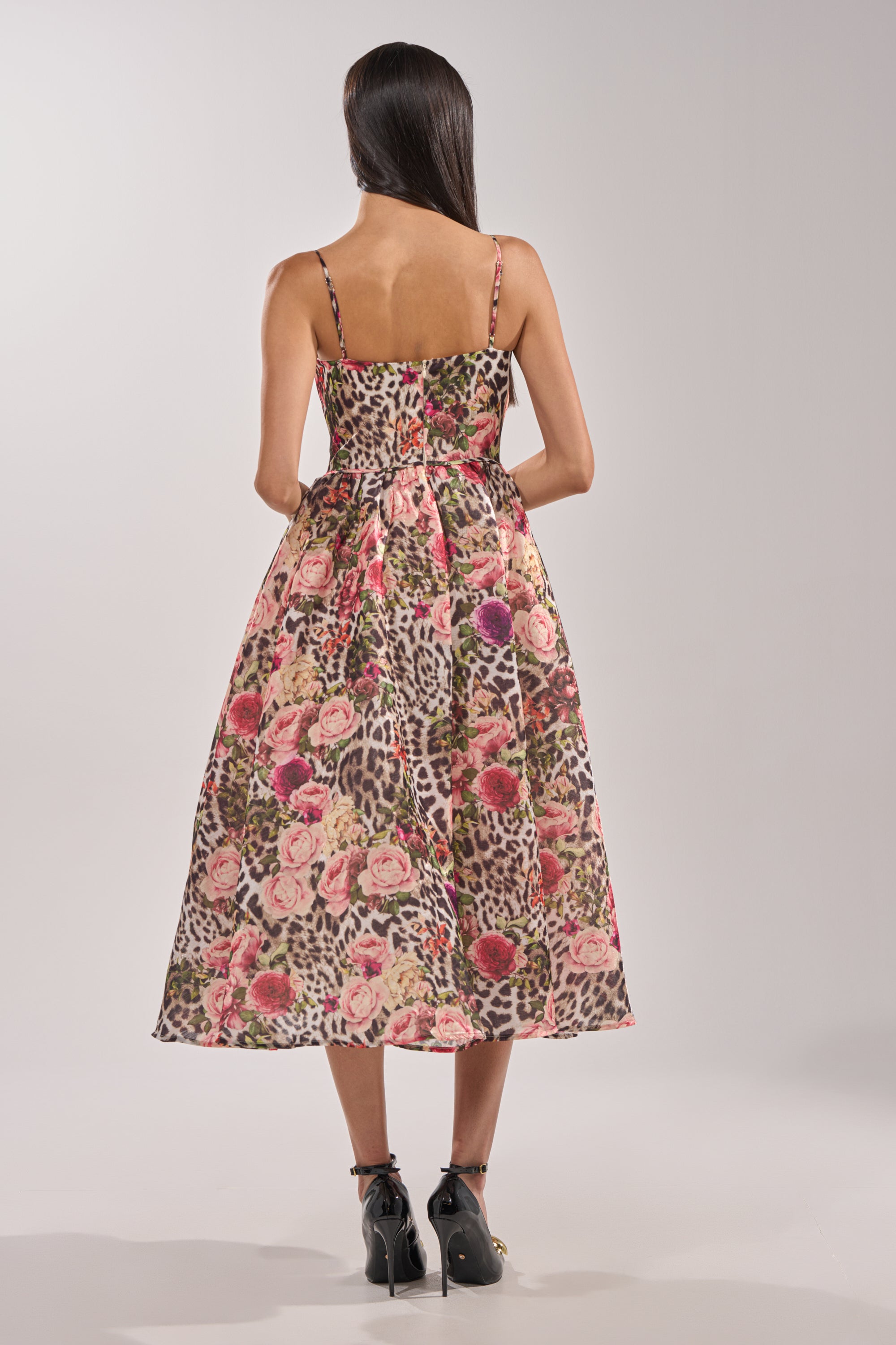 A woman with long dark hair, facing away, wears the COLETTE MAXI DRESS—sleeveless, calf-length with a leopard print and floral pattern—styled with black ankle boots against a plain light background. 4