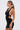 A woman in side profile wears the sleeveless DANCING QUEEN BEADED MINI DRESS, featuring a sparkly black finish, open back, and cut-out sides. She has long straight hair in a low ponytail, dangling earrings, and holds a small handbag against a white background.