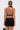 A woman with her hair in a sleek ponytail is seen from the back, wearing the DANCING QUEEN BEADED MINI DRESS and holding a small gray handbag against a plain white background.