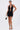 A woman poses in the DANCING QUEEN BEADED MINI DRESS, featuring an open back, plunging neckline, and front cutout. She holds a small handbag, wears black high heels, and has her hair styled back.