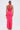 A woman with long hair in a low ponytail wears the BRIGHT AS THE SKY MESH MAXI DRESS—a bright pink halter dress with sheer panels and back slit—holding a gold clutch against a plain white background.