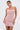A woman models the PEARL QUEEN MINI DRESS, a sleeveless, fitted pink party dress with sparkling bead details. She accessorizes with matching earrings and wears her hair back, posing against a plain white background.