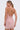 A woman in the PEARL QUEEN MINI DRESS—sparkly light pink mesh with strappy details and an open back—wears her hair in a low ponytail, standing against a plain white background.