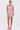 A woman poses against a white background in the PEARL QUEEN MINI DRESS, featuring pink sparkle details and thin straps, paired with pink strappy heels. Her hair is pulled back as she looks at the camera with arms relaxed by her sides.