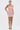A woman wears the PEARL QUEEN MINI DRESS—a sleeveless, fitted light pink party dress with thin straps and textured fabric—paired with matching pink lace-up heels, standing against a plain white background.