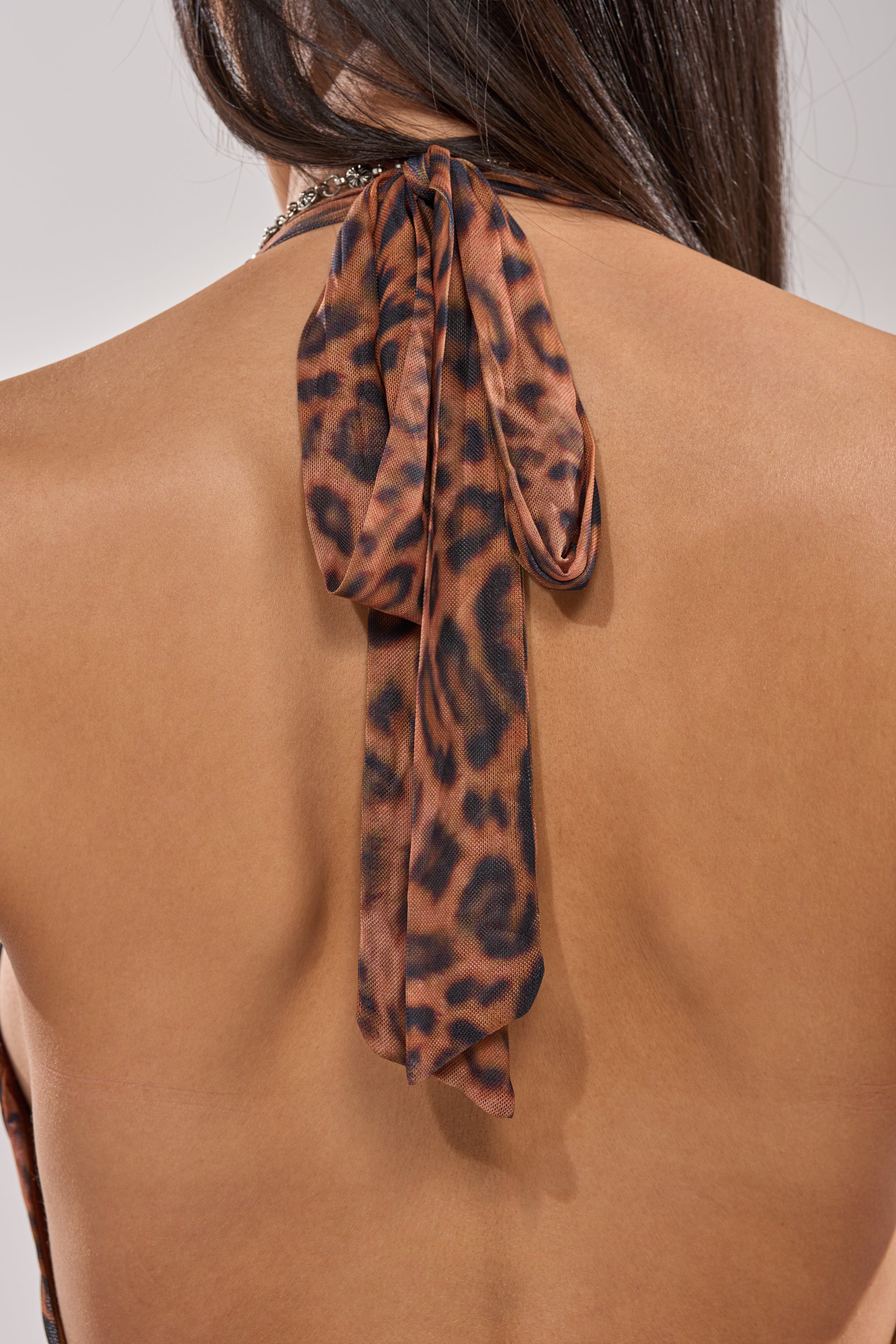 A close-up of a woman's bare back reveals the WALK ON THE WILD SIDE LEOPARD PRINT MIDI DRESS, featuring a brown and black halter-neck tie and long dark hair partly visible. 6