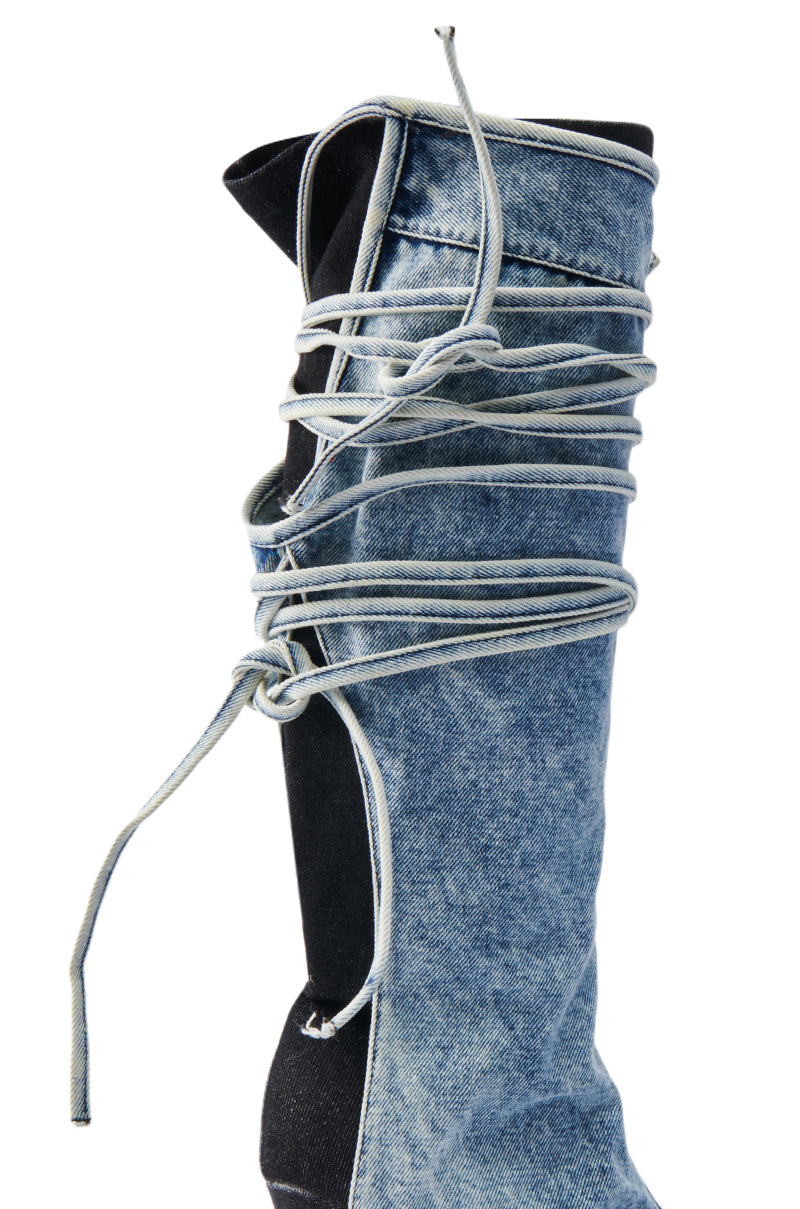 The AZALEA WANG VILLAREAL DENIM BOOT WITH TIES features knee-high denim, an intricate lace design around the shaft contrasting with black fabric, and loosely tied laces on a white backdrop for a unique and stylish look.