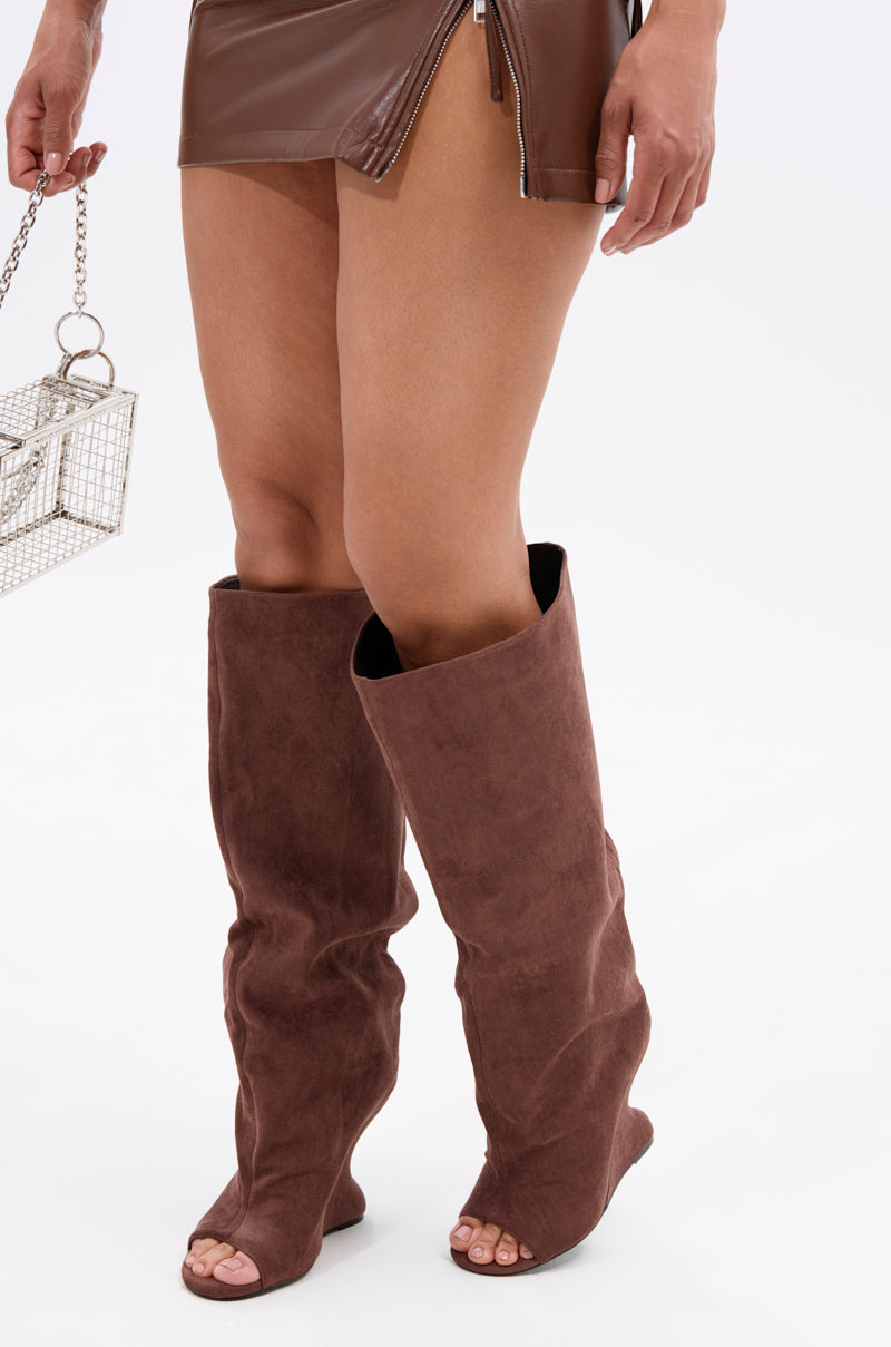 Someone wears a brown faux leather mini skirt with a front zipper and knee-high AZALEA WANG VINCENT BROWN SUEDE OPEN TOE BOOTS. They carry a small, box-shaped silver handbag with a chain handle.