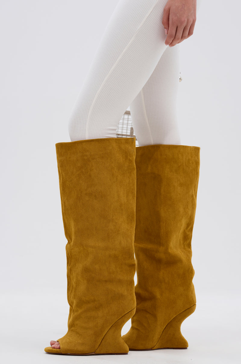 A person models the AZALEA WANG VINCENT MUSTARD SUEDE OPEN TOE BOOT, featuring a knee-high shaft, paired with white ribbed leggings. Only the lower half of their body is visible against a white background.
