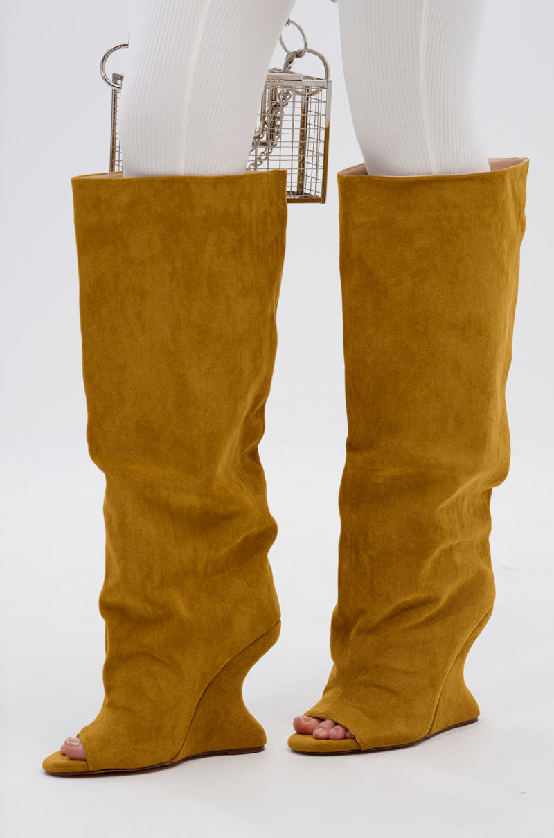Someone wearing the AZALEA WANG VINCENT MUSTARD SUEDE OPEN TOE BOOT with knee-high shafts over white ribbed tights and carrying a small silver cage-shaped handbag.
