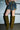 A person stands in front of a garage door, wearing AZALEA WANG VINCENT OLIVE FAUX SUEDE OPEN TOE WEDGE BOOTS and a denim-camouflage mini skirt with visible pockets and belt details.