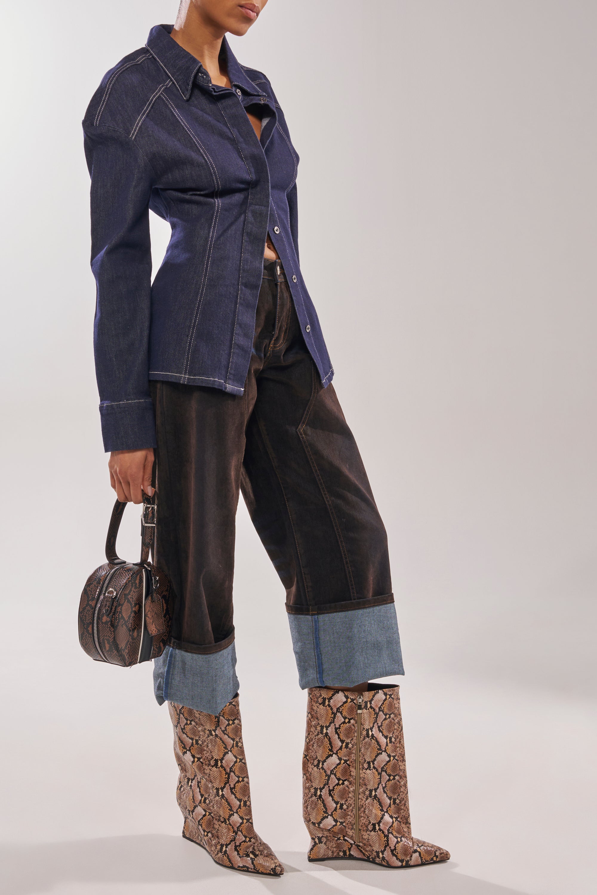 A person wears a dark denim shirt, wide dark jeans with large cuffs, and AZALEA WANG VINCI SNAKE PU PRINT WEDGE BOOTIE knee-high snakeskin booties. They carry a matching small snakeskin handbag. The person's face is not visible. 3