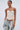 A woman wears the LETS GET ROWDY LACE UP CORSET in cream, styled with light blue distressed jeans and a patterned bandana at her waist, standing against a plain light background.