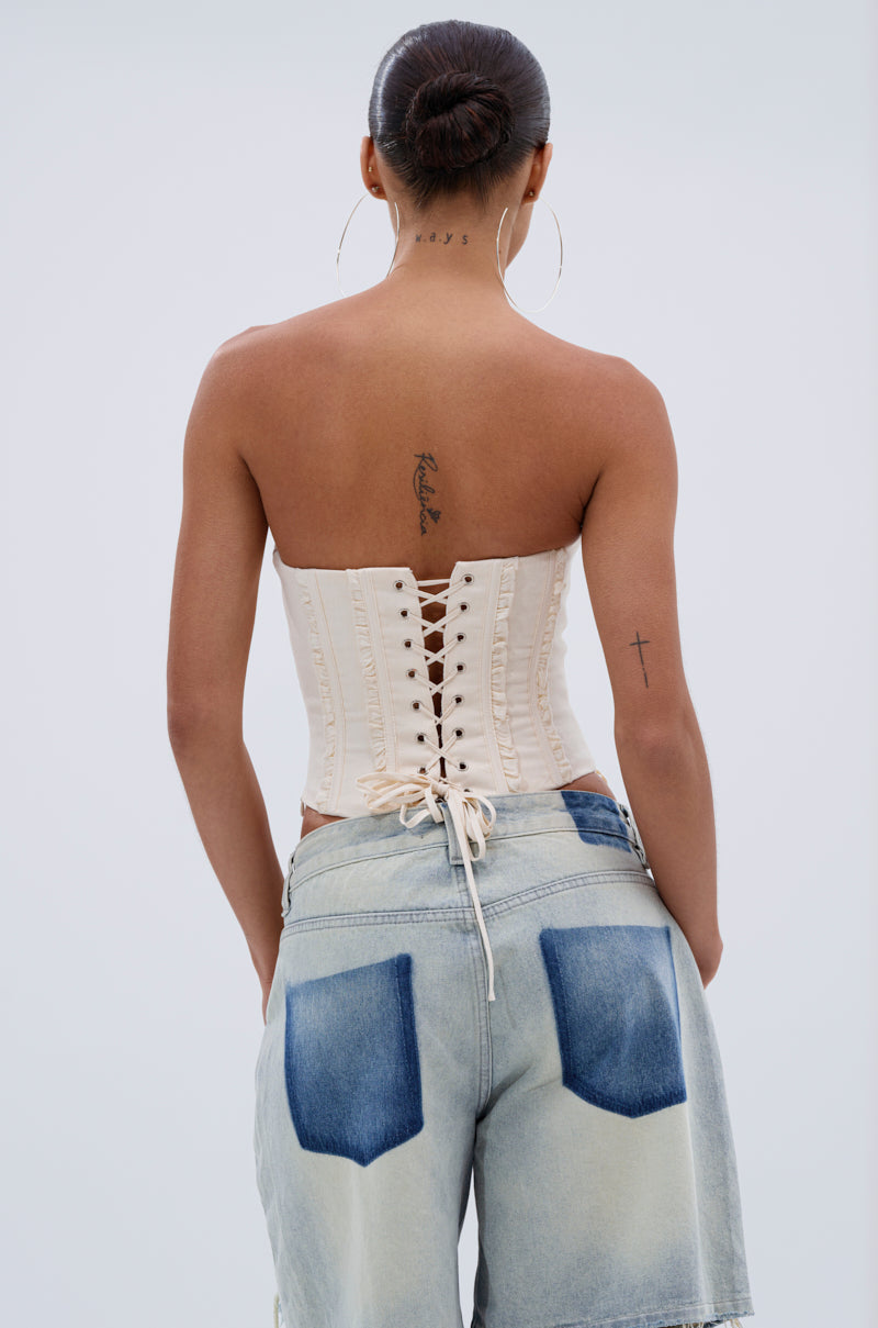 A person with a bun hairstyle, hoop earrings, and tattoos on their upper back and left arm wears the LETS GET ROWDY LACE UP CORSET and loose, light-washed denim shorts with dark back pockets, seen from behind. 3