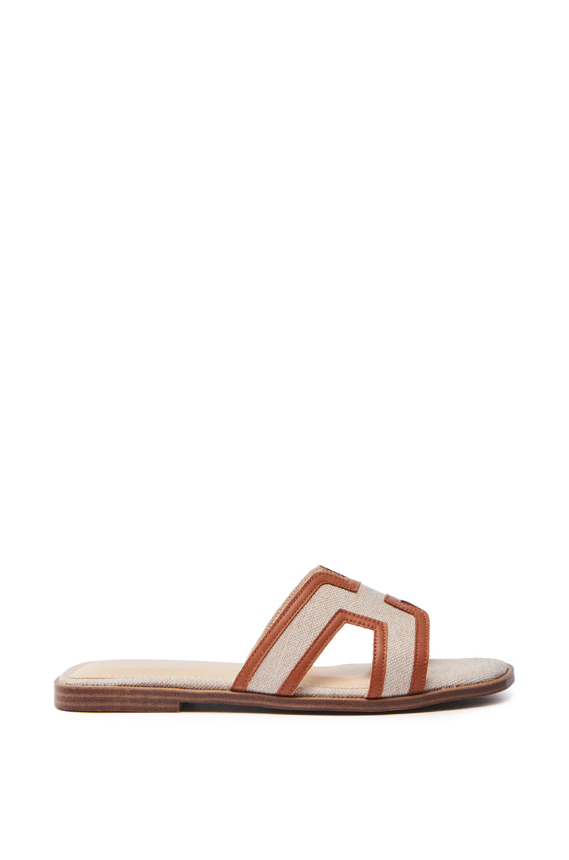 The AKIRA VITTORIA BEIGE SANDAL is a flat slide with an elegant wooden sole, featuring an open square toe and a woven textile strap adorned with beige and brown geometric cut-outs, beautifully showcased against a white background.