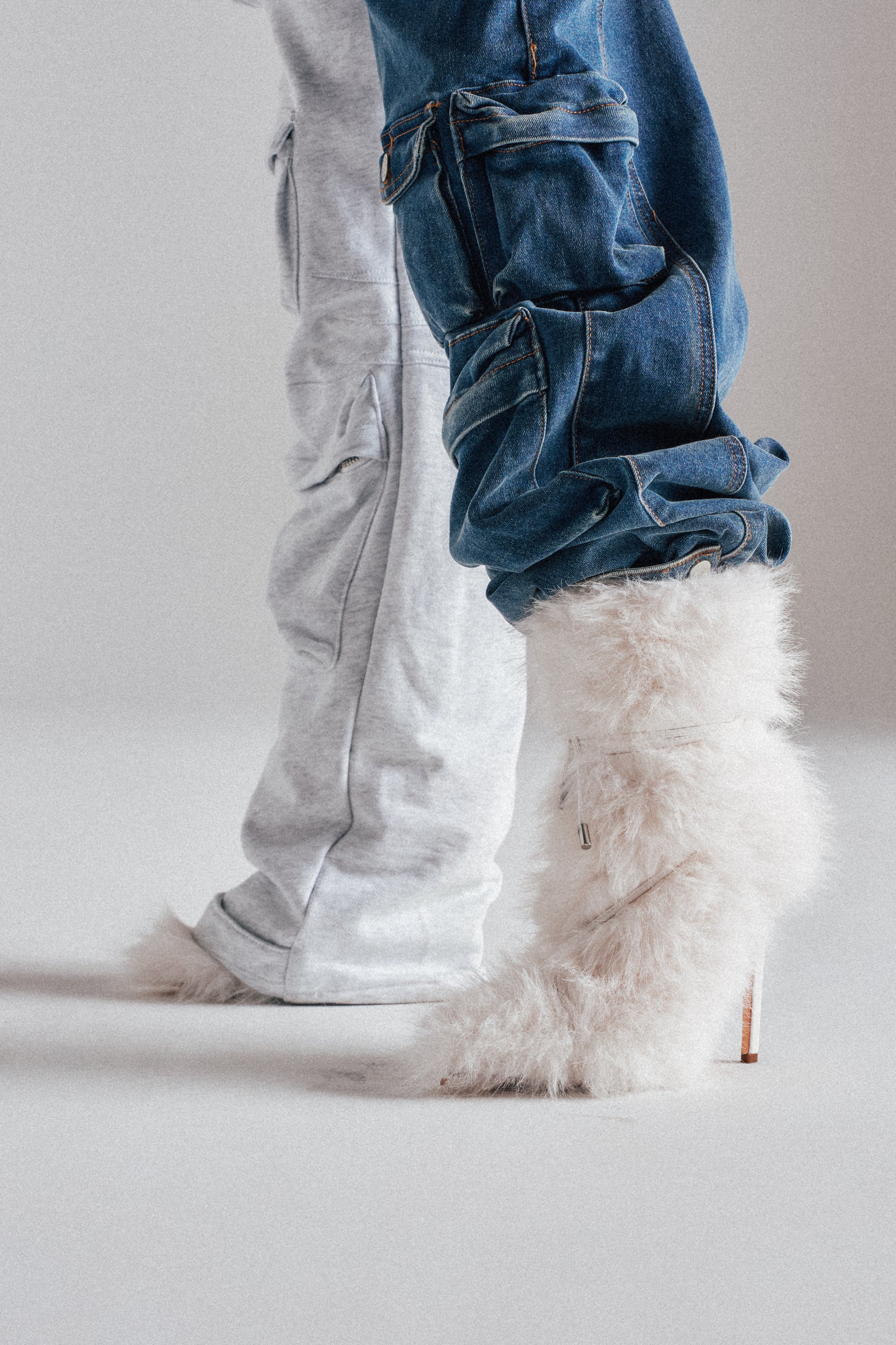 Two people stand side by side. One wears light gray sweatpants and fuzzy slippers, while the other sports blue jeans and the AZALEA WANG VITYA IVORY FUR BOOTIE with a stiletto heel. The photo highlights their lower legs and footwear.