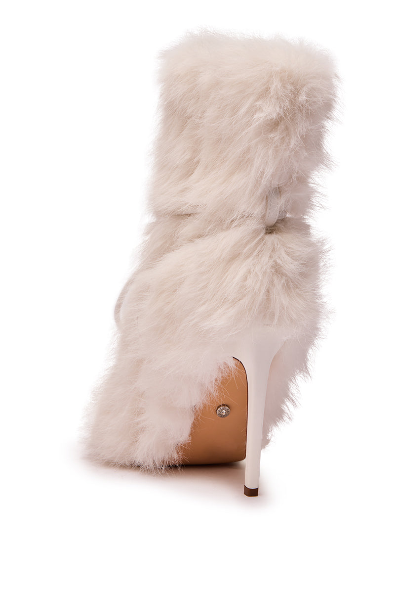 The AZALEA WANG VITYA IVORY FUR BOOTIE features a high heel, mid-calf shaft, fluffy white faux fur, slim white stiletto heel, and tan sole—shown from the back and slightly to the side on a white background.
