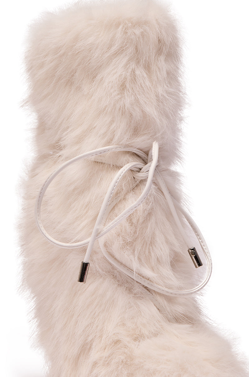 A close-up of the AZALEA WANG VITYA IVORY FUR BOOTIE, a tall, fluffy off-white mid-calf boot with soft faux fur texture and white laces wrapped around the shaft, featuring metallic lace tips.