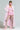 A person confidently poses while wearing the VIVIAN FUR TRIM COAT, featuring a pink feathered design and a quilted satin lining. They complement the coat with a pink ruffled dress, patterned white tights, and pink furry shoes. With braided hair and unique pink sunglasses, they exude a stylish, modern look against a plain background.