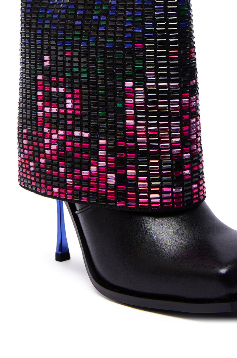 A close-up of the AZALEA WANG VOLLMER BLACK RHINESTONE CUFF BOOTIE WITH SQUARE TOE, featuring a black stiletto heel and reflective blue detail, paired with pants adorned with a grid of colorful rectangular beads.